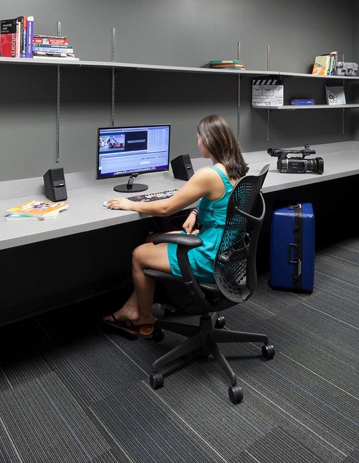 a student sits at an editing dock with a film camera by her side. 